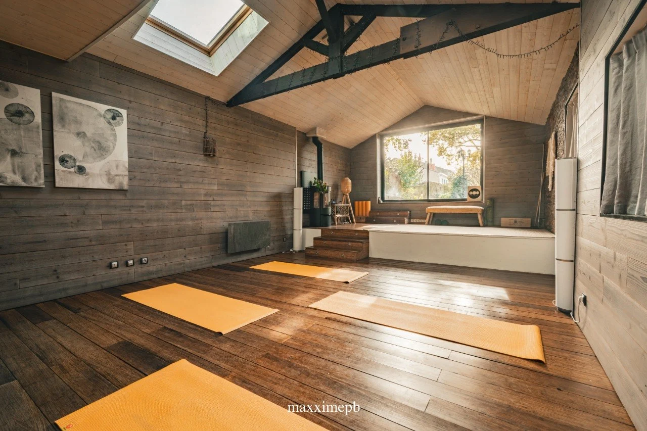 Salle de l'atelier Mimosa Pop à Bordeaux : grenier en bois clair, charpente apparente, tapis de yoga déroulés au sol, lumière naturelle par la verrière